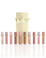 Un set de zece produse de ulei de buze P.Louise Christmas stay strălucitoare dispuse la rând în fața unei cutii de ulei de buze cilindrice auriu strălucitor, cu un capac de coroană aurie, pe un fundal alb curat. Produs lichid pentru buze Lip Oil cu un aplicator de picior de căprioară în timp ce ține tubul în cealaltă mână, așezat pe un fundal alb curat.