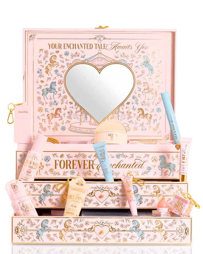 A P.Louise cutie de set cadou pentru frumusețe PR de Crăciun roz pastel, albastru și galben etichetată „Povestea ta fermecată” cu o oglindă în formă de inimă pe capac și sertare deschise, înconjurată de tuburi cosmetice asortate, sticle și o pungă mică pe un fundal alb.