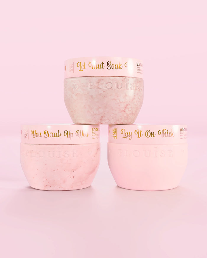 Trei recipiente roz P.Louise Hop Into Self-Care Pink Marshmallow cu săruri de baie, exfoliant de corp și unt de corp cu text auriu pe fundal roz