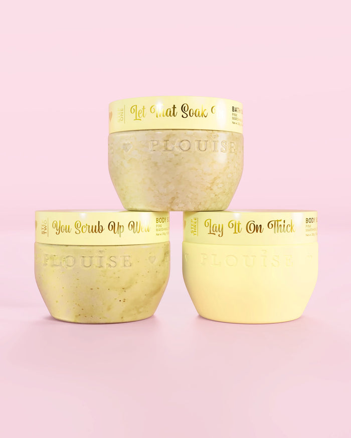 Trei recipiente galbene P.Louise Hop Into Self-Care Starwberry Shortcake cu săruri de baie, exfoliant de corp și unt de corp cu text auriu pe fundal roz