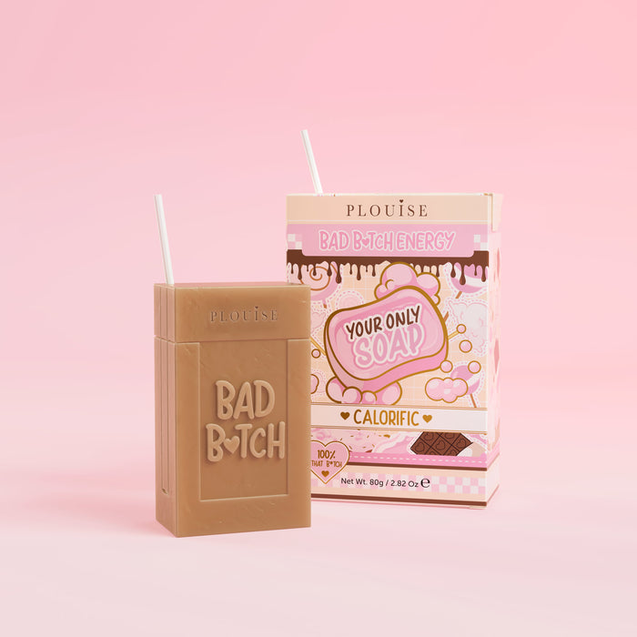 A brown bar of soap with 'Bad Bitch' engraved on it, accompanied by a colourful juice box package with 'Calorific' labelled on it, presented on a pink background.