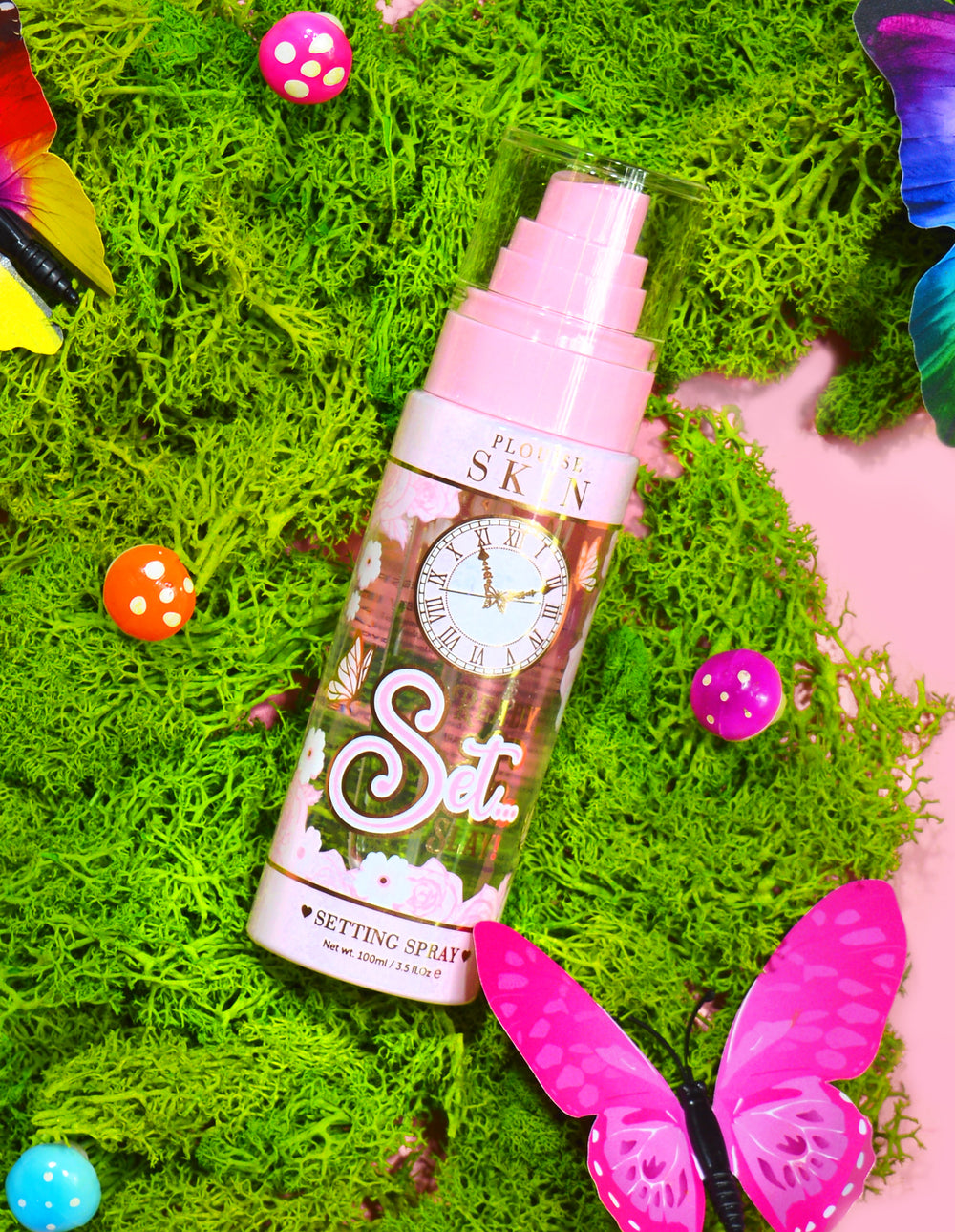 O sticlă de P. Louise Ready Set Slay Long Lasting Setting Spray, înconjurată de elemente decorative, inclusiv mușchi colorat, fluturi și ciuperci.